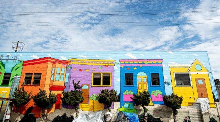 Tents line a sidewalk with a bright mural and blue sky in San Francisco