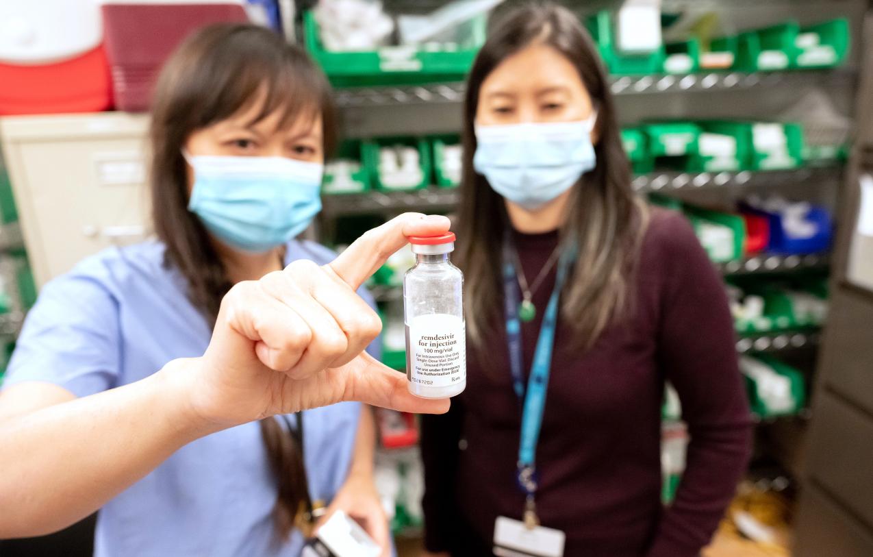 Two nurses in face masks examine a sample