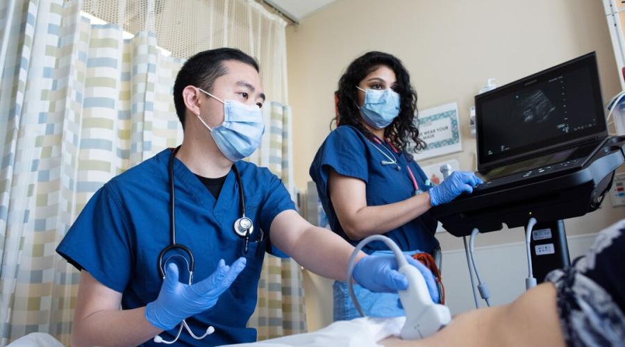 Two hospital workers perform an ultrasound on a pregnant person