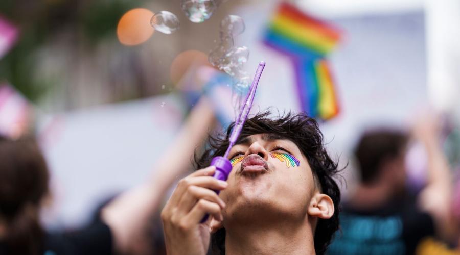 A person blows bubbles with a Pride flag in the background
