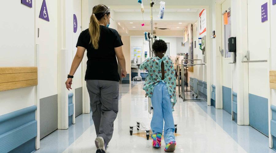 A UCSF staff member walks with a young patient around the Pediatric Oncology unit at UCSF Benioff Children's Hospital Oakland. Photo by Maurice Ramirez.