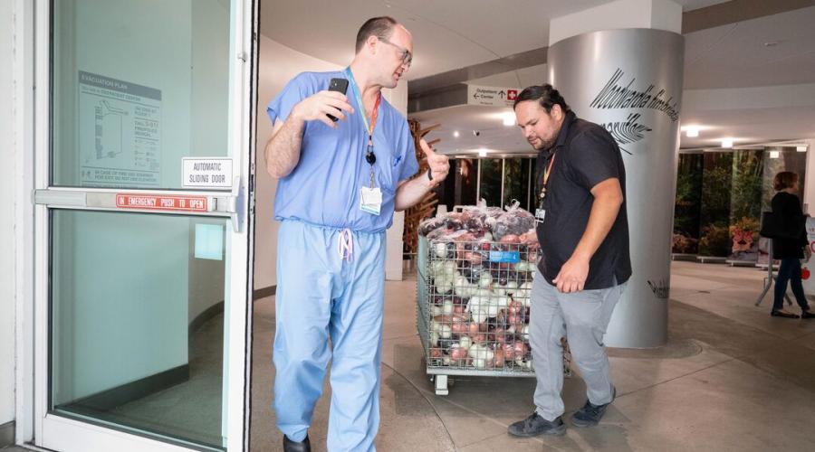 Jason Jagodzinski, MD, left, Health Sciences associate clinical professor in the UCSF Department of Orthopedic Surgery, talks with Rigoberto Del Toro, coordinator of the Food Farmacy program at UCSF Benioff Children's Hospital Oakland, as he wheels bags of groceries not picked up during the Food Farm pop-up into the hospital’s Outpatient Center lobby for staff and patient families to enjoy. Photo by Susan Merrell